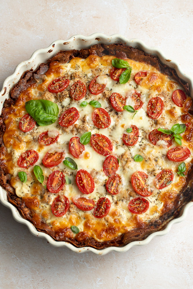 Tarte pommes de terre, thon, tomates et basilic dans un moule à tarte blanc.