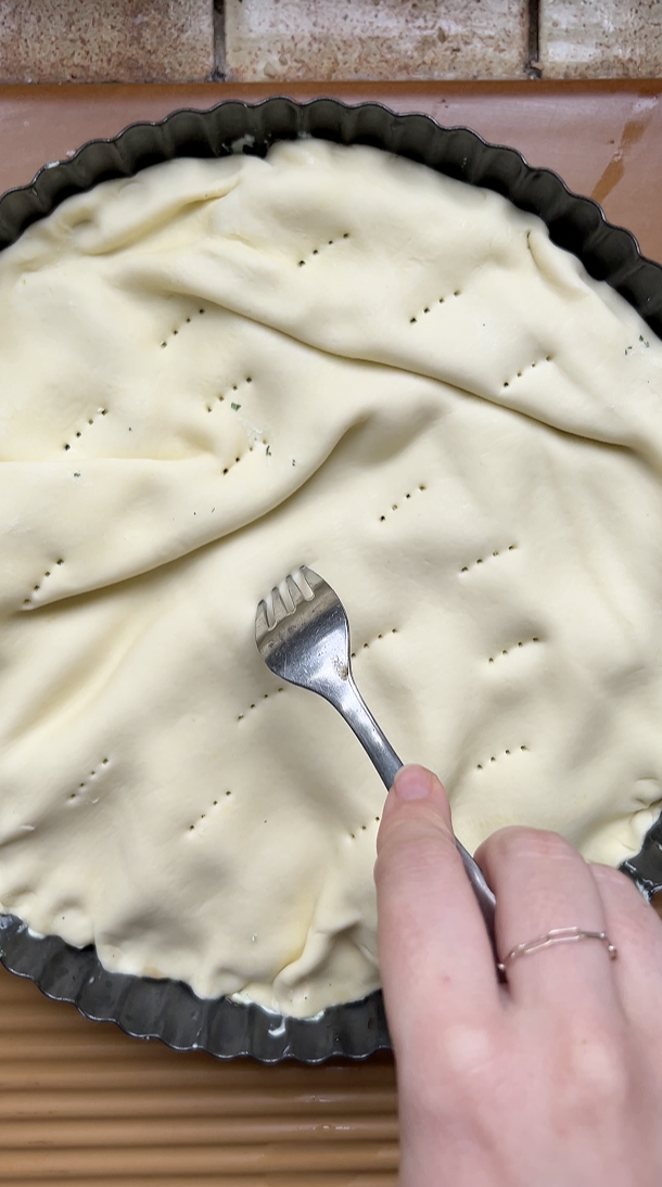 Hand holding a fork, which pricks the pastry before baking.