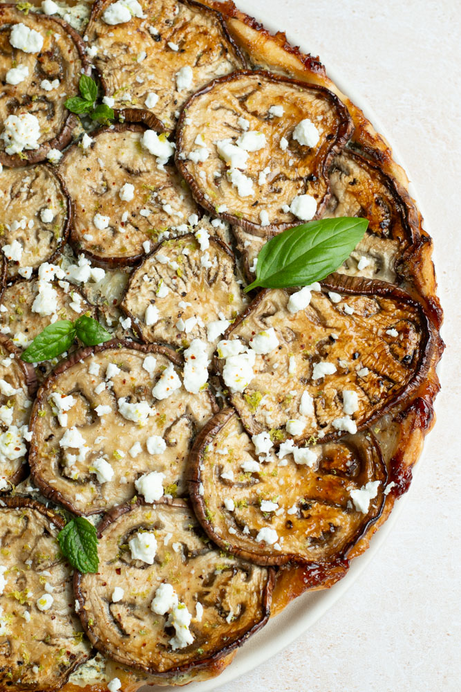 Tatin d'aubergines dans une assiette avec des feuilles de basilic, un demi citron vert et une serviette.