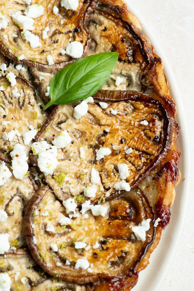 Eggplant tatin on a plate with basil leaves, half a lime and a napkin.