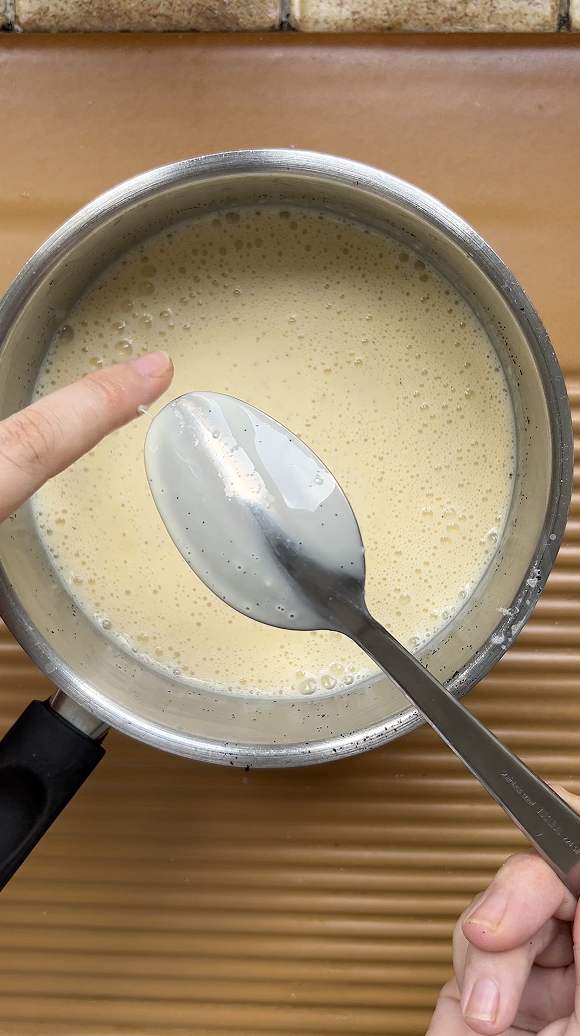 Doigt qui fait un trait sur le dos d'une cuillère à soupe, nappée de crème anglaise.