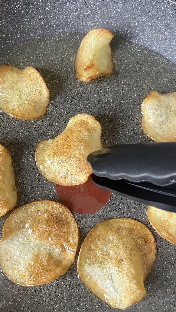 A pair of tongs that turn the chips as they cook, in the frying pan of frying oil.