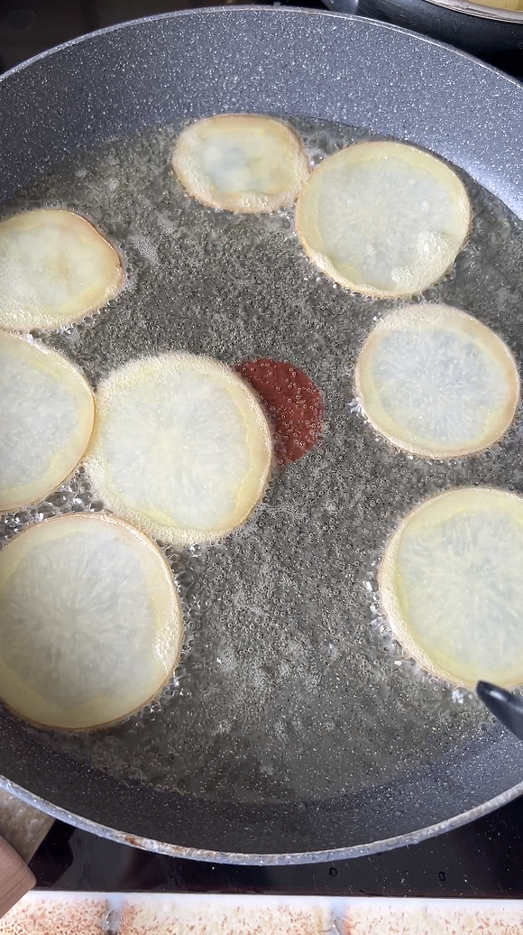 Potato slices cooked in a pan of frying oil.