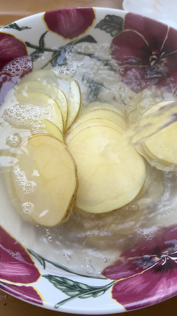 Boiling water poured over potato slices in a large bowl.