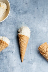 Scoops of vanilla ice cream in two cones and a bowl. Two other cones at bottom right.