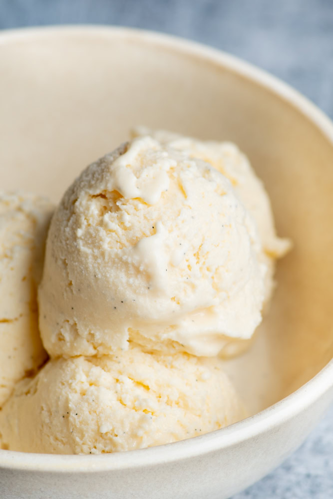 Scoops of homemade vanilla ice cream in a beige bowl.