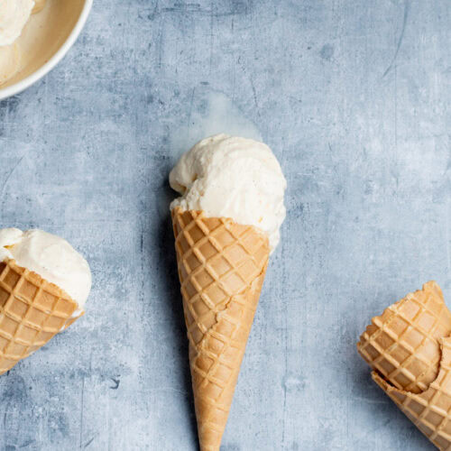 Scoops of vanilla ice cream in two cones and a bowl. Two other cones at bottom right.