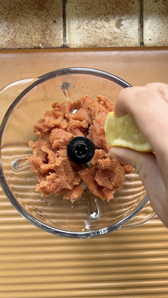 Oeufs de cabillaud fumés dans un blender avec une main qui presse un demi citron.