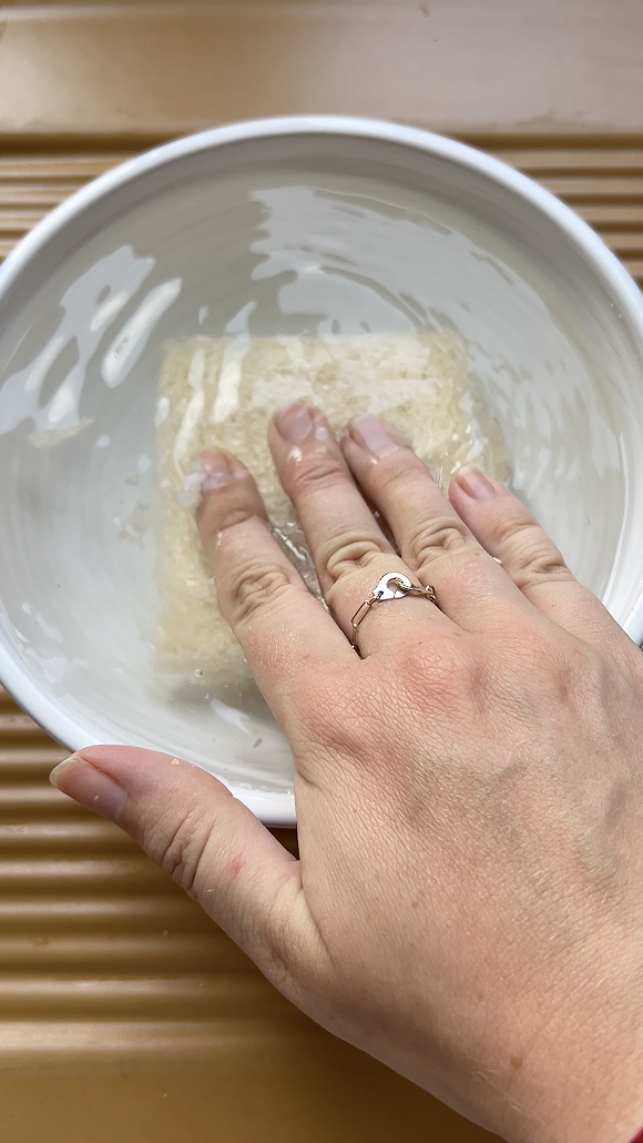 Une main qui trempe plusieurs tranches de pain de mie dans un grand bol d'eau.