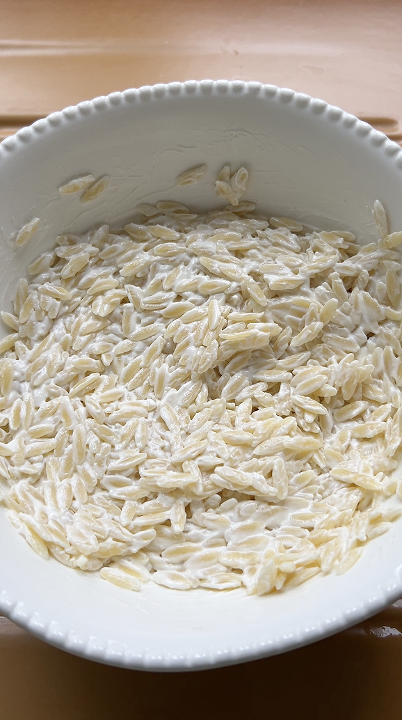 Pâtes Orzo dans un grand saladier blanc, mélangées avec du fromage frais.