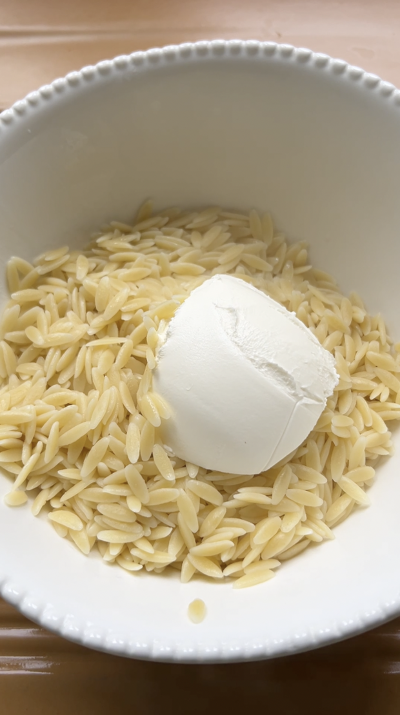 Orzo pasta in a large white bowl, with cream cheese.