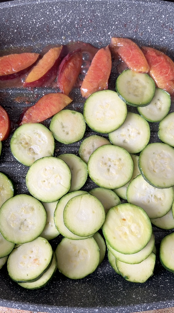 Zucchini strips and peach quarters cooking in a frying pan.