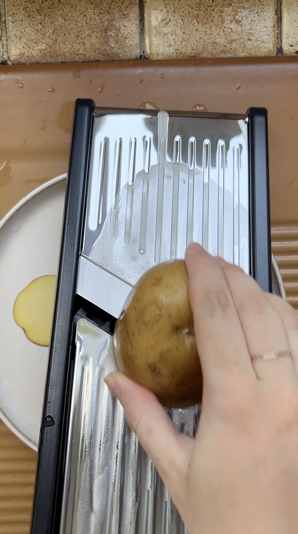 A potato held in one hand and passed over a mandolin to make very thin slices.