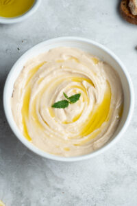 Homemade tarama in a large white bowl with a drizzle of olive oil and a mint leaf.