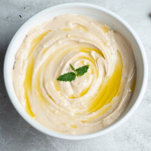 Homemade tarama in a large white bowl with a drizzle of olive oil and a mint leaf.