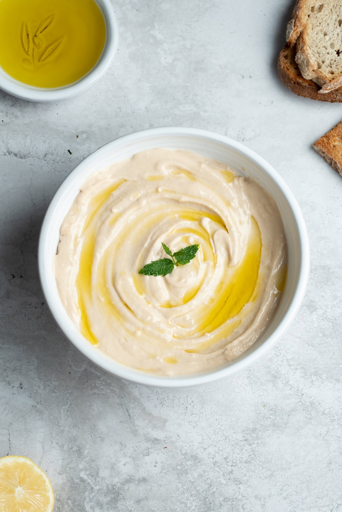 Tarama maison dans un grand bol blanc avec un filet d'huile d'olive et une feuille de menthe, des tranches de pain et un demi citron.