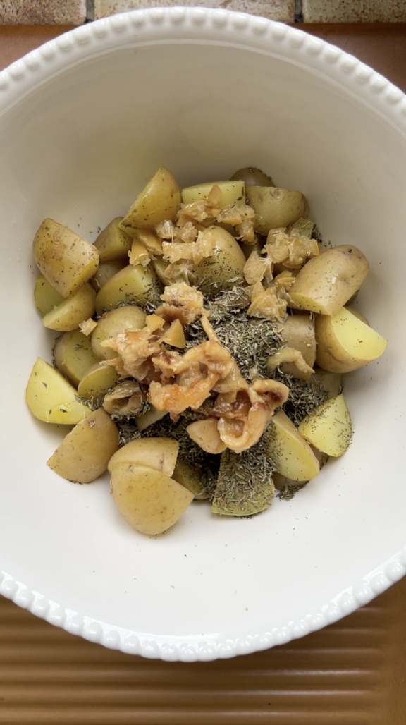 Potatoes in a large white bowl with thyme, preserved garlic and pieces of preserved lemon.