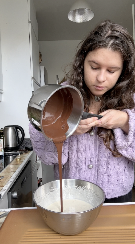 Marie pouring the pan of melted chocolate into the brown sugar and egg mixture.