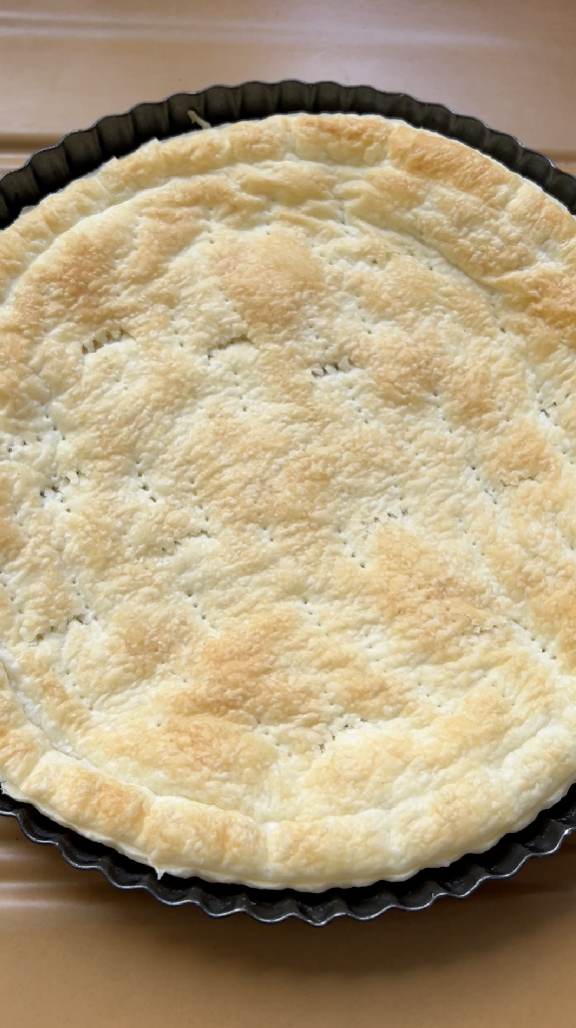 Puff pastry in a black tart tin with small holes, after baking.