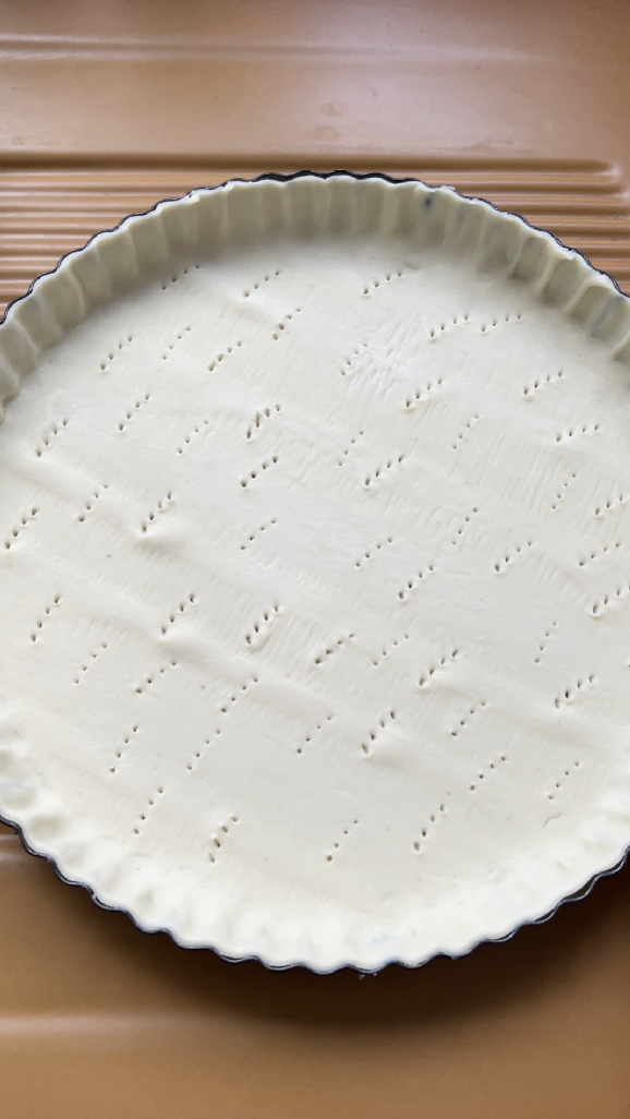 Pâte feuilletée dans un moule à tarte noire avec des petits trous, avant sa cuisson.