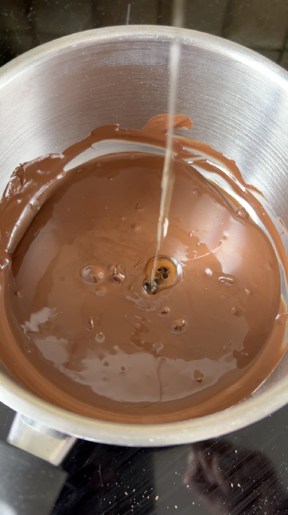 Filet d'huile neutre versé dans la casserole de chocolat fondu.