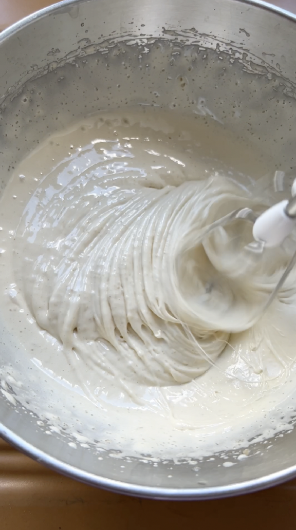 Eggs and brown sugar beaten in a stainless steel bowl to form a creamy white mixture.