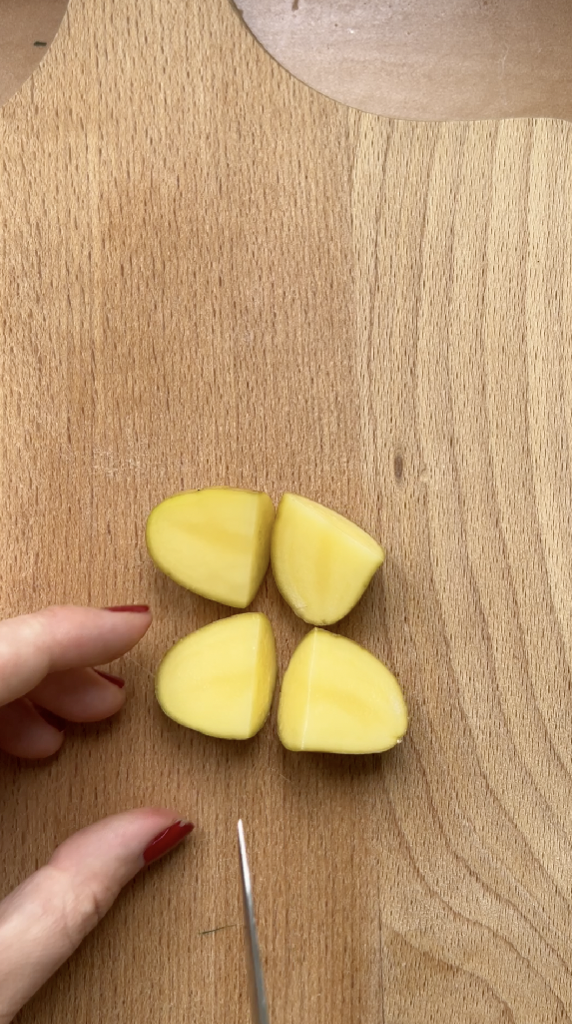 A potato cut into quarters by a knife, on a wooden board.