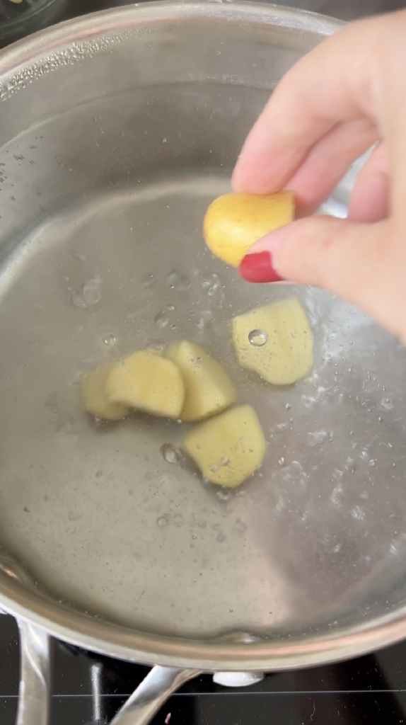 Hand throwing cut potatoes into a pan of boiling water.