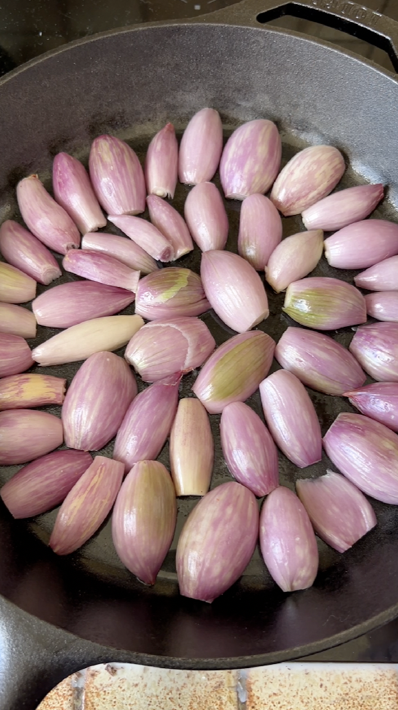 Halved shallots cooking in a black frying pan with butter.