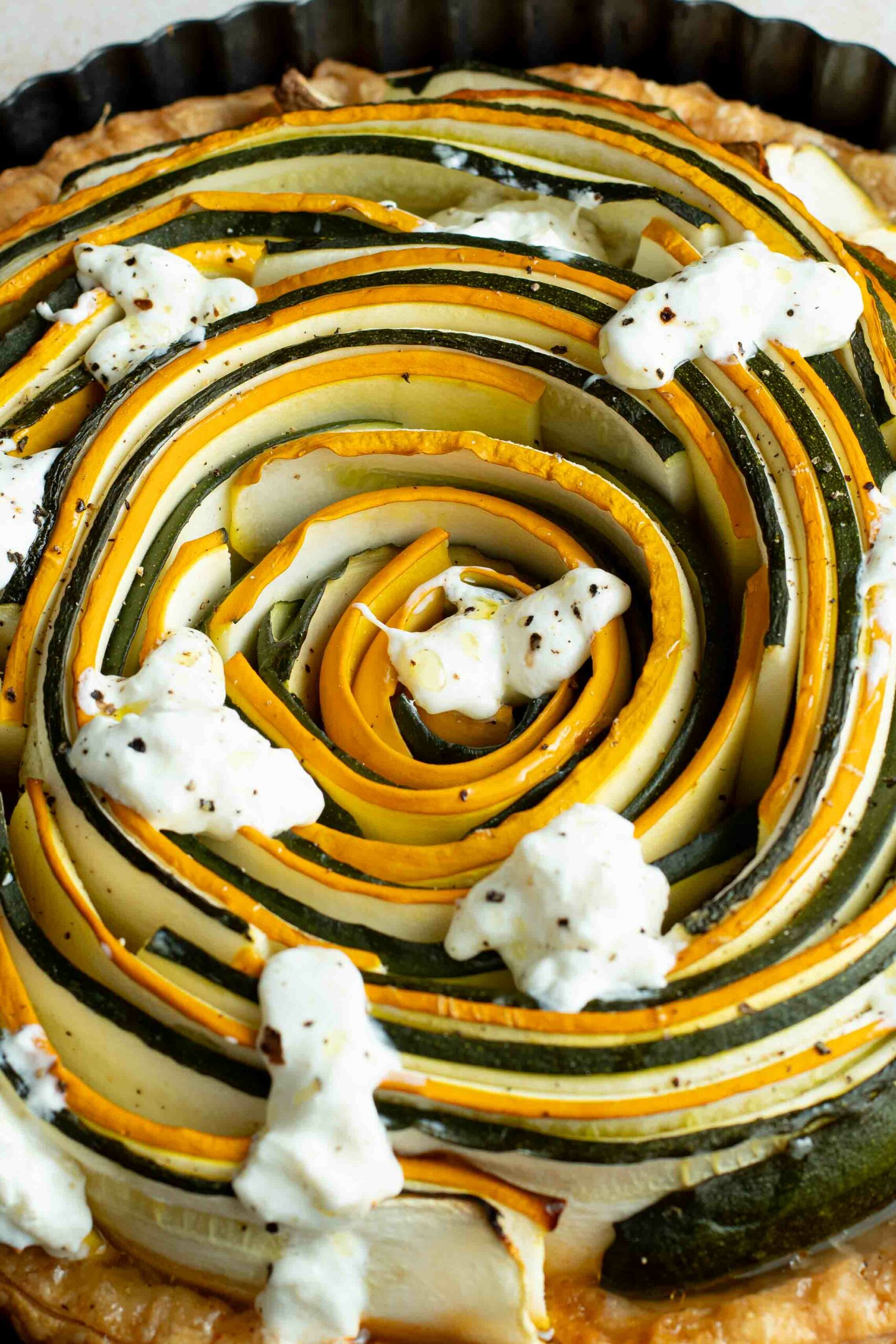 Green and yellow zucchini spiral tart with pieces of burrata.