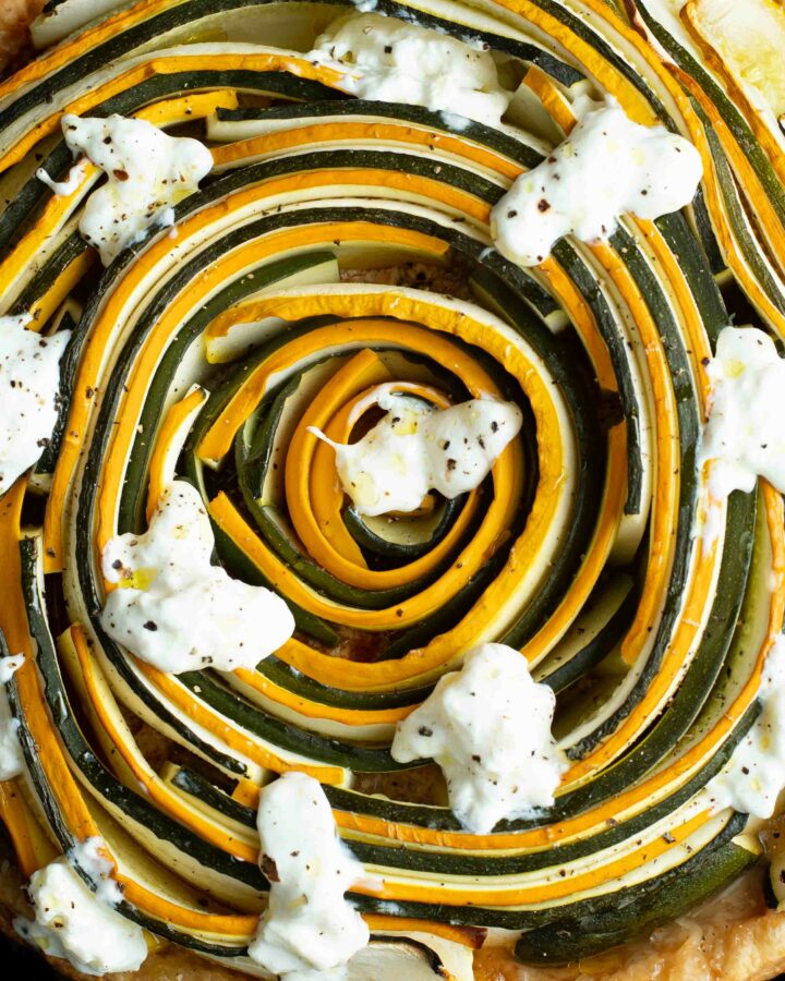 Green and yellow zucchini spiral tart with pieces of burrata.