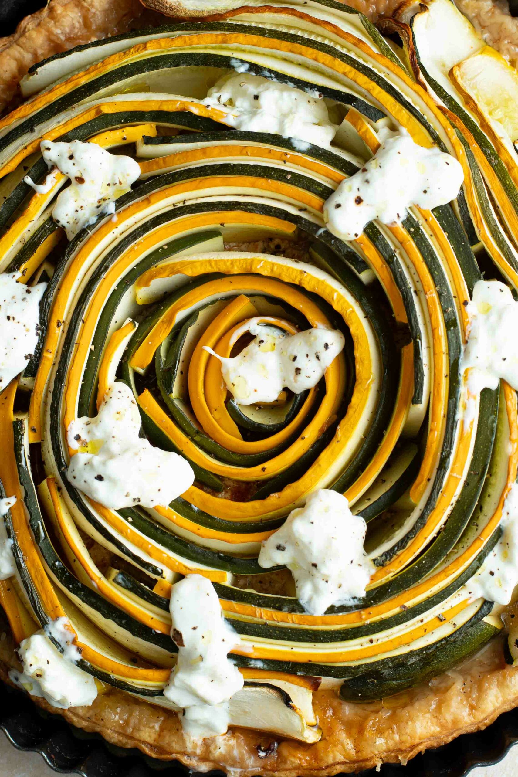 Green and yellow zucchini spiral tart with pieces of burrata.