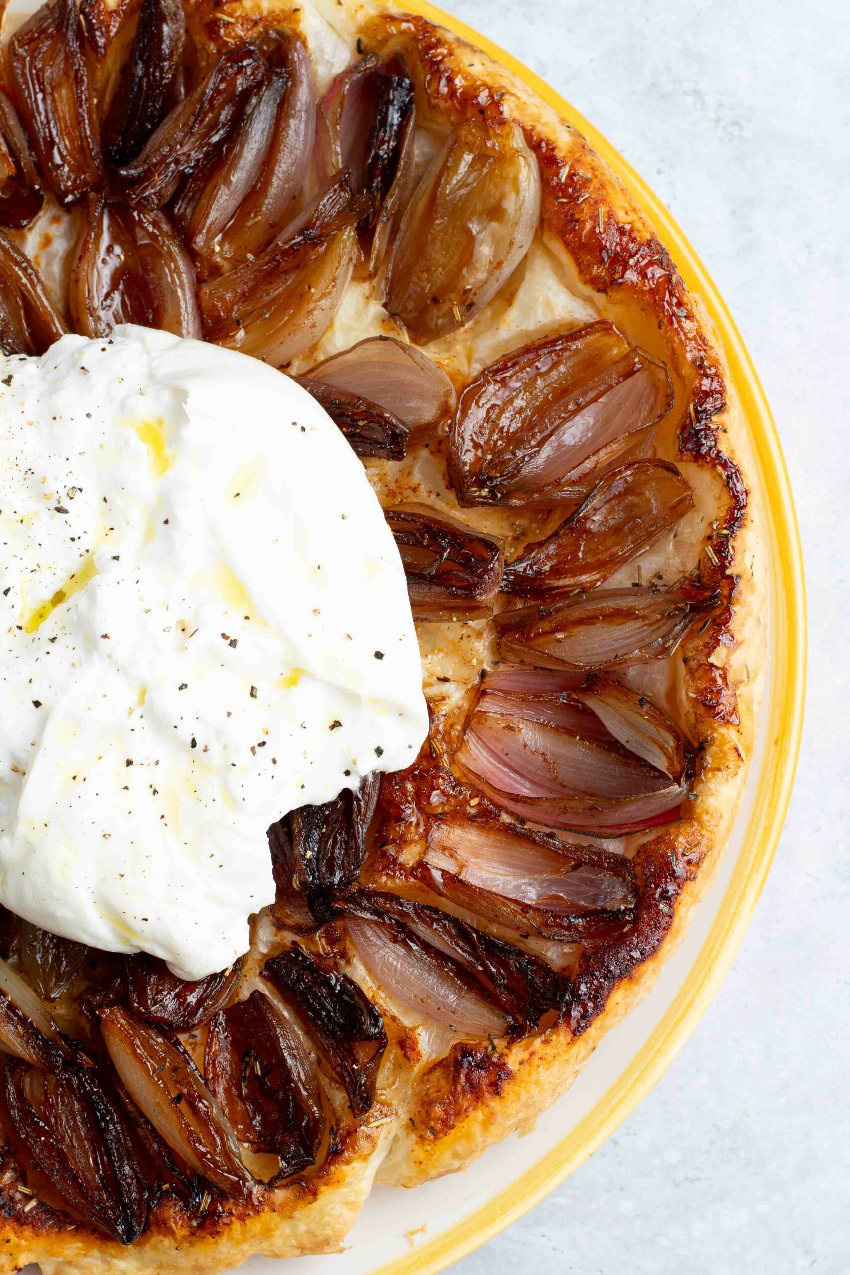 French tart tatin with caramelized shallots in a yellow and white dish, with a large burrata cheese on top.