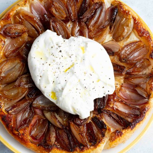 Tatin d'échalotes caramélisées dans un plat jaune et blanc, avec une grande burrata sur le dessus.