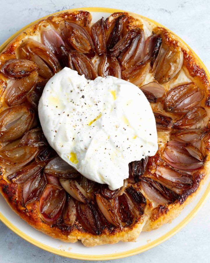 Tatin d'échalotes caramélisées dans un plat jaune et blanc, avec une grande burrata sur le dessus.