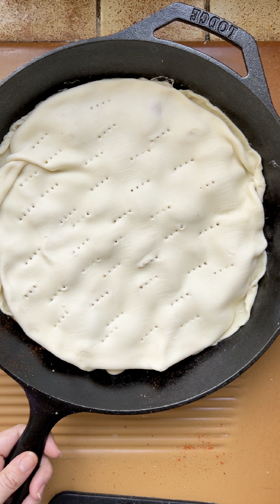 Puff pastry placed on the shallots in the black pan.