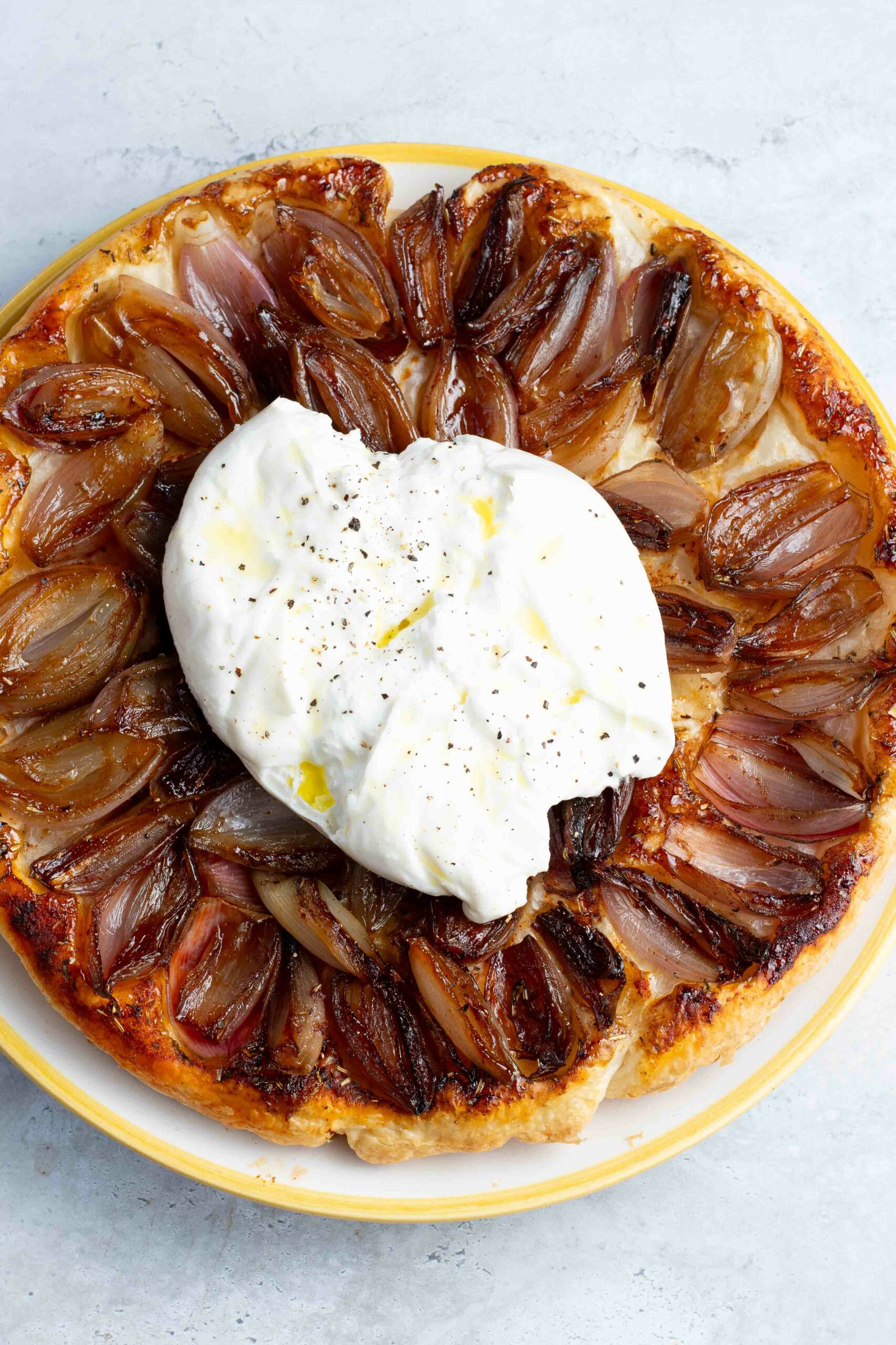 Tatin d'échalotes caramélisées dans un plat jaune et blanc, avec une grande burrata sur le dessus.