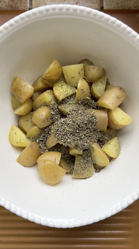 Potatoes in a large white bowl with thyme.