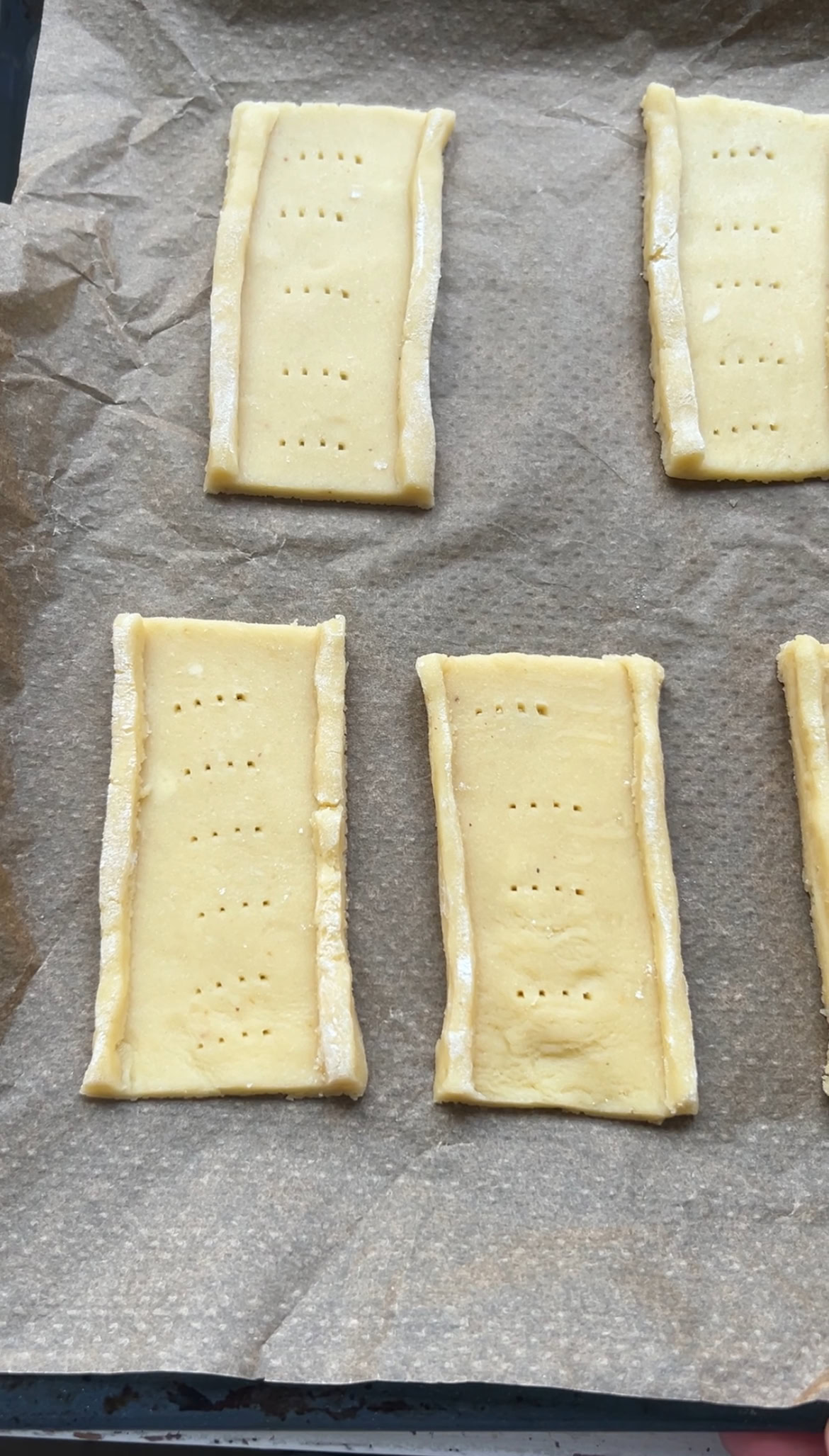 M&Ms shortbread biscuits on a baking sheet lined with parchment paper, poked with a fork.