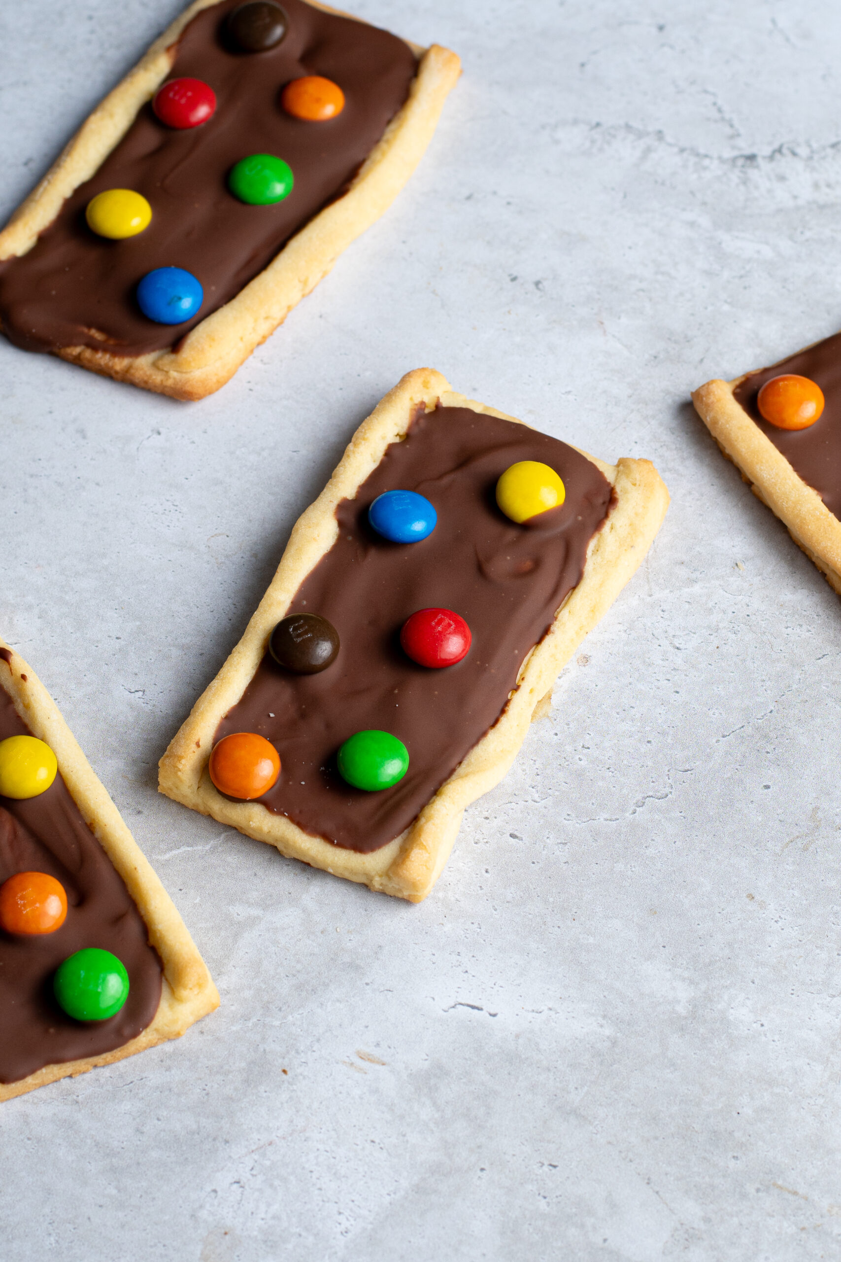 Several chocolate M&Ms shortbread biscuits on a gray work surface.