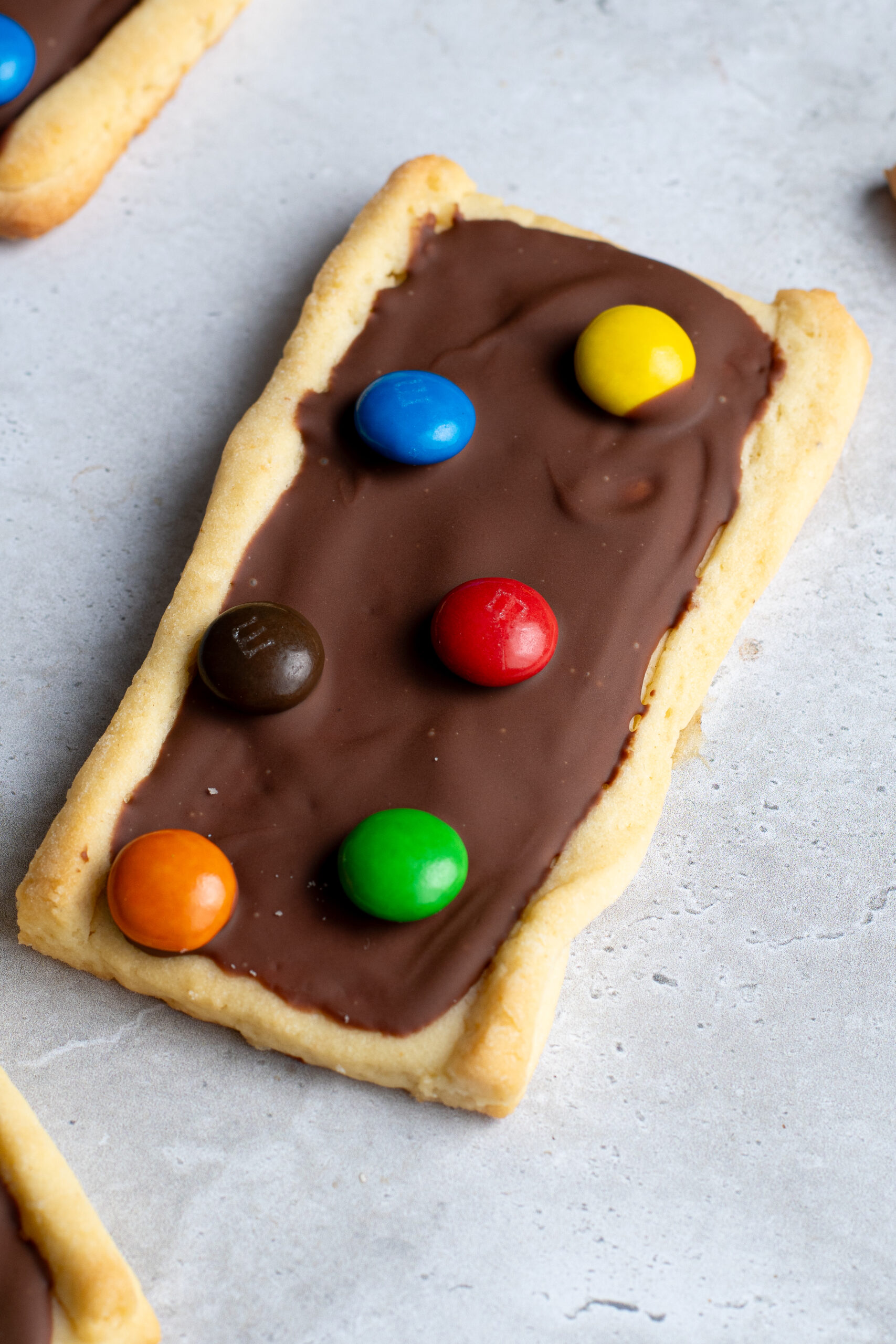 Several chocolate M&Ms shortbread biscuits on a gray work surface.