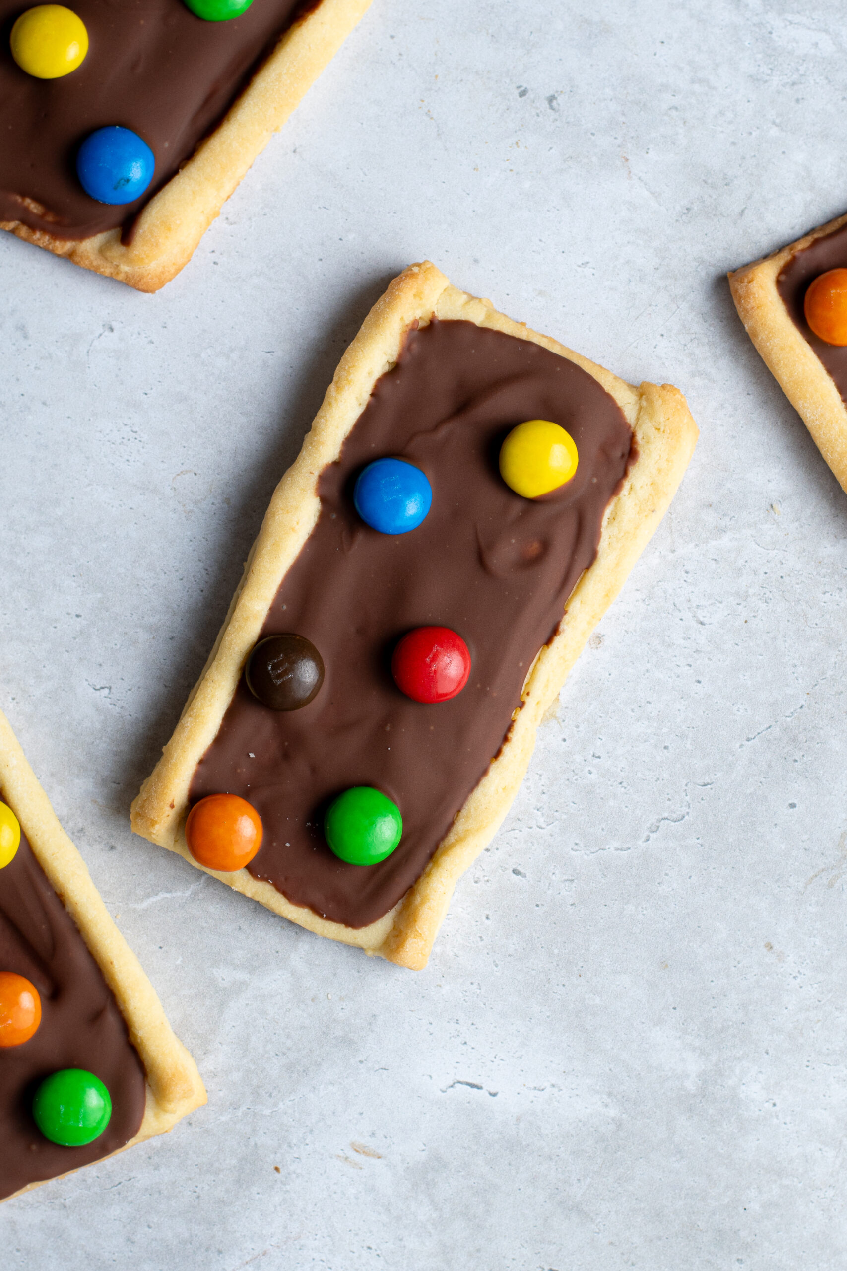 Several chocolate M&Ms shortbread biscuits on a gray work surface.