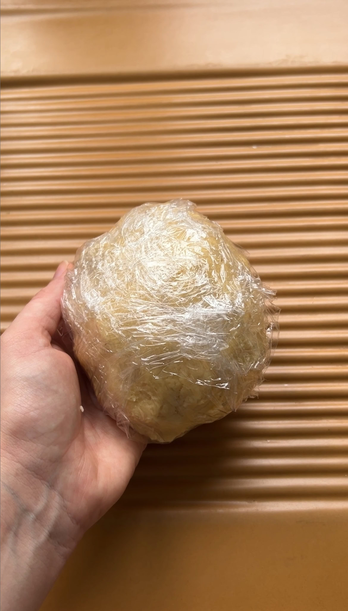 Dough ball wrapped in plastic wrap, held by a hand.