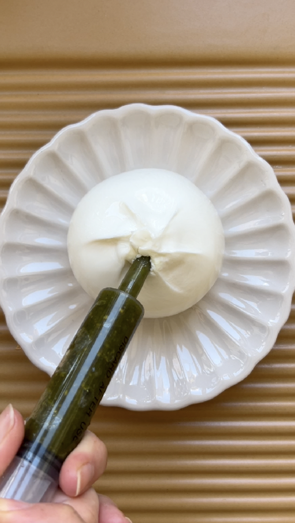 A food syringe filling the burrata with pistachio pesto.