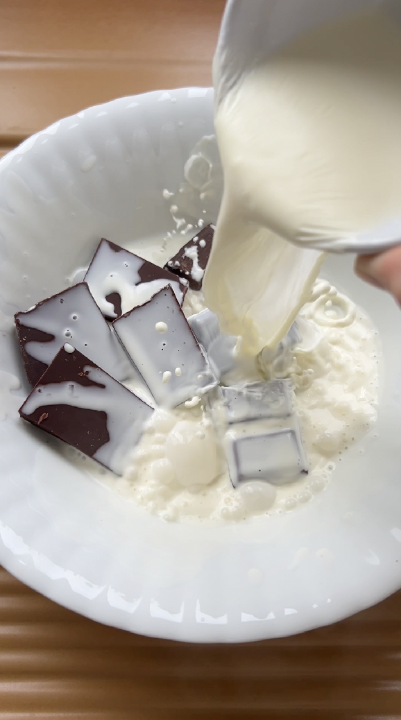 Heavy cream poured over dark chocolate pieces in a white bowl.