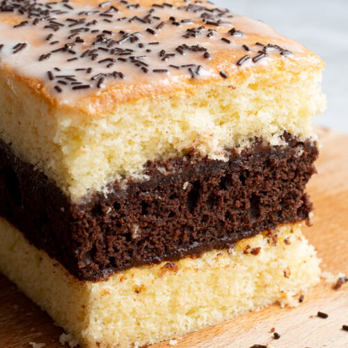 Soft, homemade French layered chocolate and vanilla sponge cake on a wooden board.