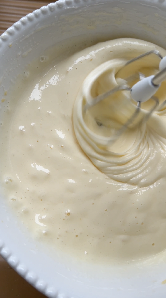 Eggs and sugar in a white bowl, mixed with an electric mixer.