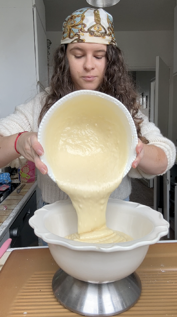 Marie pours the batter into a white bowl and weighs it on a scale.