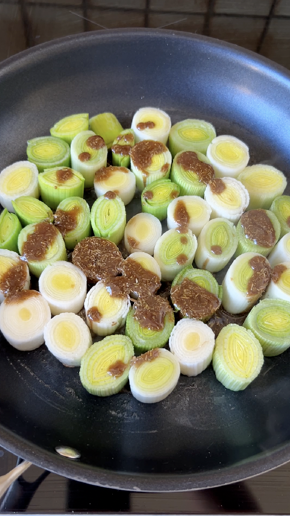 Leek sections cooking in a pan, with the sauce poured over them.