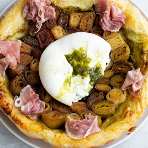 Tatin de poireaux sur une assiette avec une burrata fourrée au Pesto de pistache et du jambon de Parme.